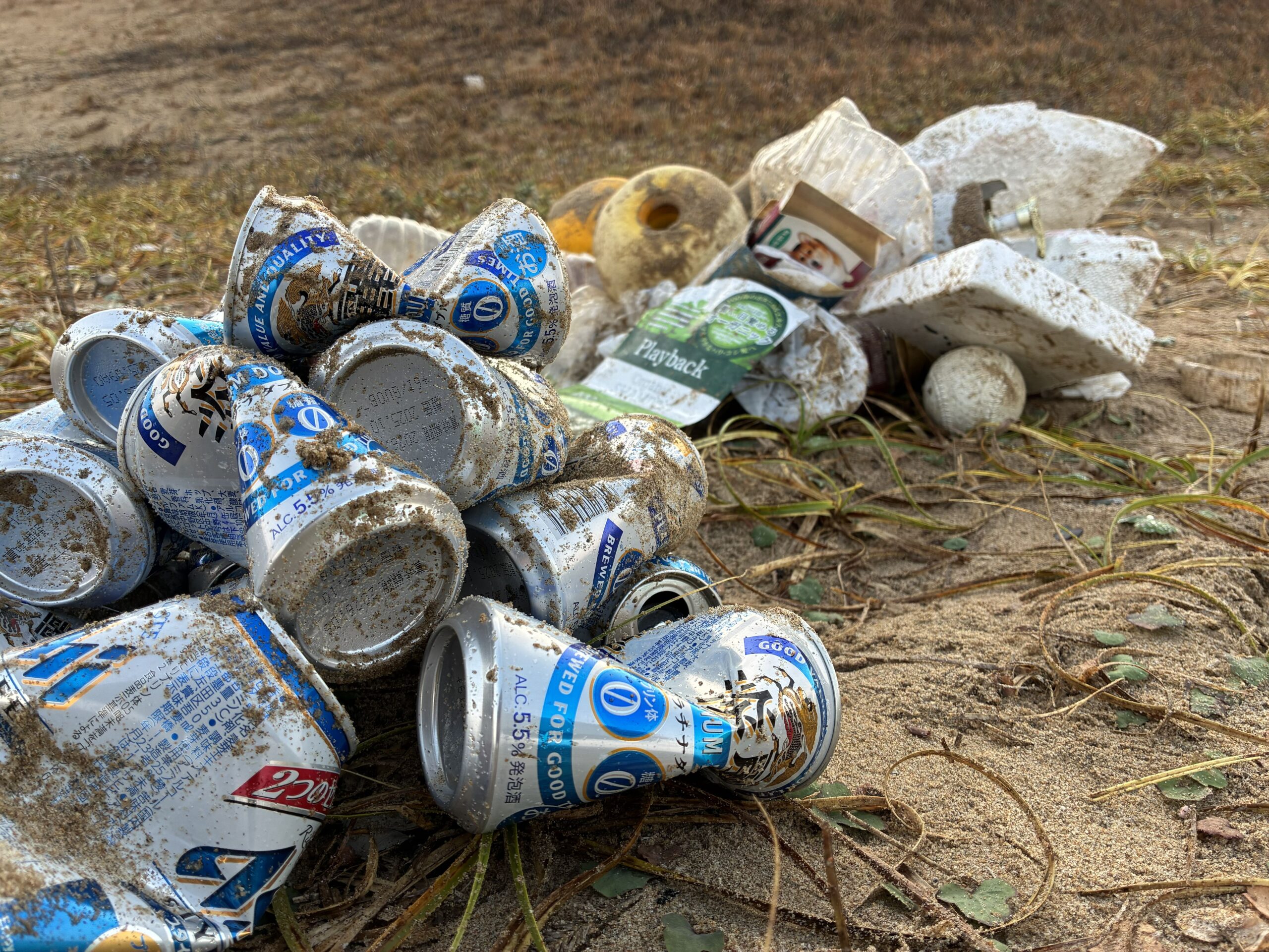 手前には海岸清掃で回収した大量の缶ビールと、奥には大量のプラスチック製品